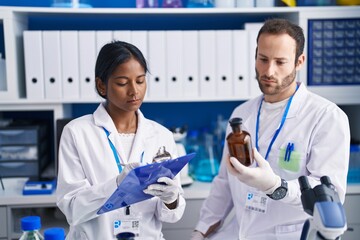 Man and woman scientists holding bottle writing report at laboratory