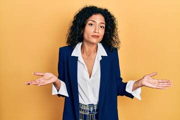 Young latin girl wearing business clothes clueless and confused expression with arms and hands...