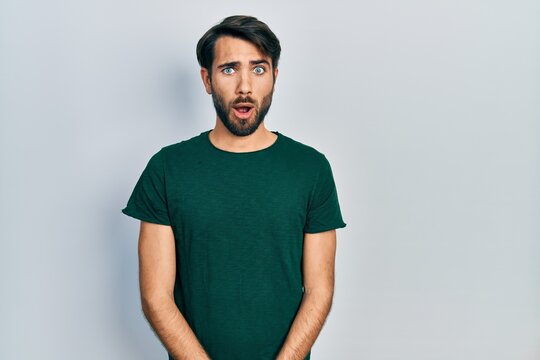 Young hispanic man wearing casual white tshirt afraid and shocked with surprise expression, fear and excited face.