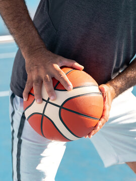 Closeup image of hands of adult basketball player holding a orange sport ball at waist level ready to pass it