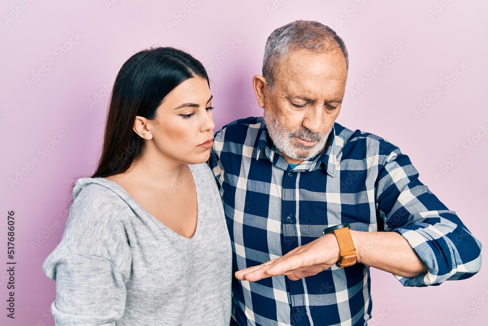 Wall mural Hispanic father and daughter wearing casual clothes checking the time on wrist watch, relaxed and confident