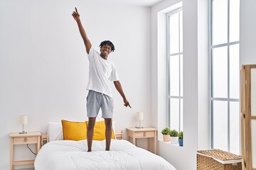 Fototapeta na wymiar African american man smiling confident standing on bed at bedroom