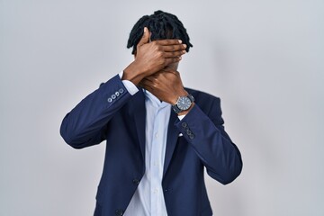 Young african man with dreadlocks wearing business jacket over white background covering eyes and...