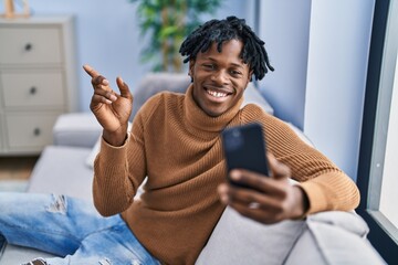 Young african man with dreadlocks using smartphone doing video call smiling happy pointing with...