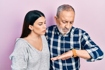 Hispanic father and daughter wearing casual clothes checking the time on wrist watch, relaxed and confident