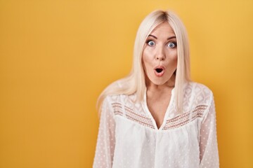 Caucasian woman standing over yellow background scared and amazed with open mouth for surprise, disbelief face