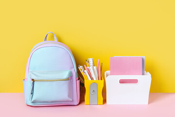 Blue backpack with school stationery on yellow  background. Office supplies with school bag on the table. Concept back to school.