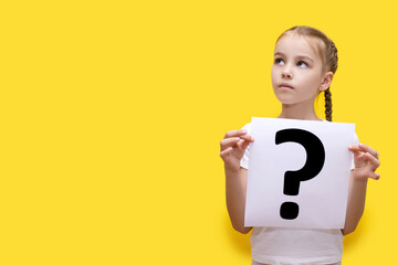 Girl child holding a sheet of paper with a question mark on a yellow background. The concept of...