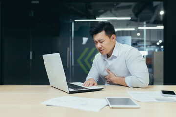 Fototapeta premium Sick Asian businessman at work, man chest pain heart, overworked and depressed boss.