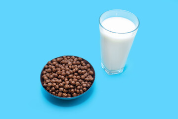 Corn chocolate flakes in the form of balls in a bowl and a glass of milk on a blue background. American style fast and healthy breakfast concept. Carbohydrate food with calcium flakes