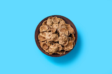 Brown corn flakes in a bowl on a blue isolated background in the center of the image. Flakes with chocolate flavor close-up top view. American style energy carbohydrate breakfast