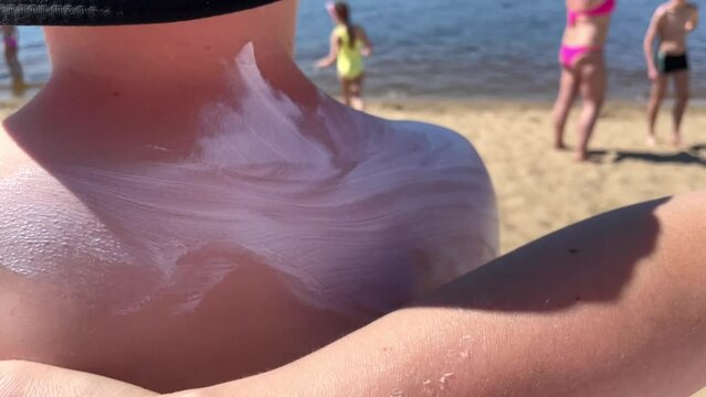 Close-up of a mother applying protective sunscreen or suntan lotion to her son's shoulder to take care of her baby's delicate skin near the sea or river