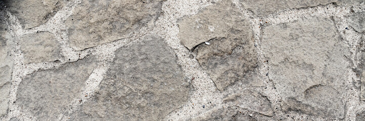Stone pavement. Texture of stone paved ground. Large jagged stone blocks on a pedestrian sidewalk or road. Ancient masonry. Wide panoramic texture for background and design.