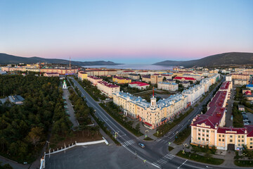 Aerial view of a seaside town. Top view of the streets and buildings. In the distance the sea bay and mountains. Beautiful morning cityscape. City of Magadan, Magadan region, Far East of Russia.