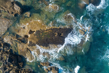 Top view of sea waves crashing on a rocky shore, aerial shot