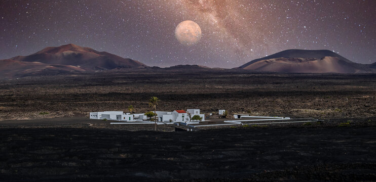 Amazing nocturnal panoramic landscape of volcano craters in Timanfaya national park. Full moon over La Gueria, Lanzarote island, Canary islans, Spain. Artistic night sky picture