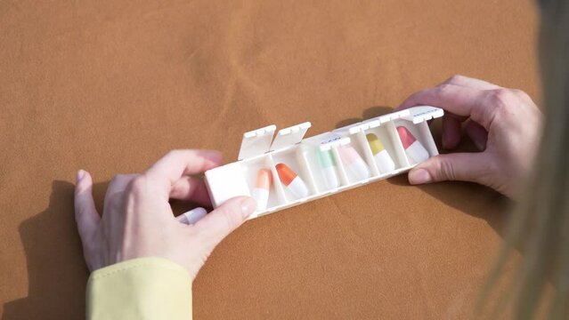 Female hand sorting pills in pillbox on brown background