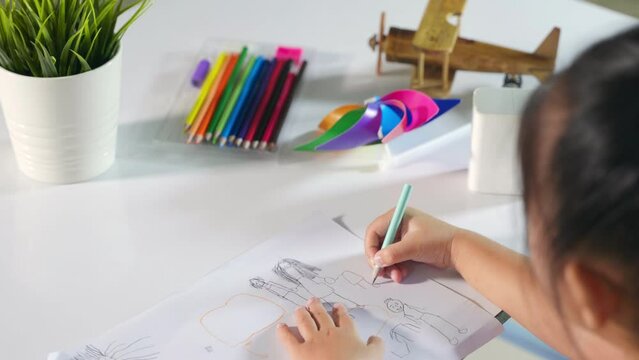Asian cute kid preschooler sitting on table smiling she draw and writing picture with pencil at home to learning arts homework, Happy child little girl drawing cartoon on paper before paint the color