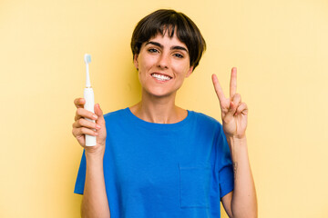 Young caucasian woman holding a electric toothbrush isolated on yellow background showing number two with fingers.