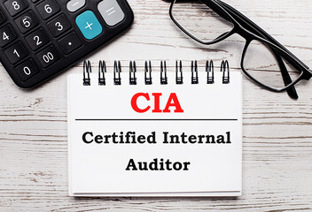 On a light wooden table calculator, glasses and a blank notepad with the text CIA Certified Internal Auditor. Business concept - obrazy, fototapety, plakaty