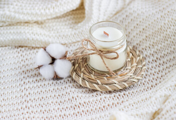 Handmade candle with cotton flower on white cozy blanket