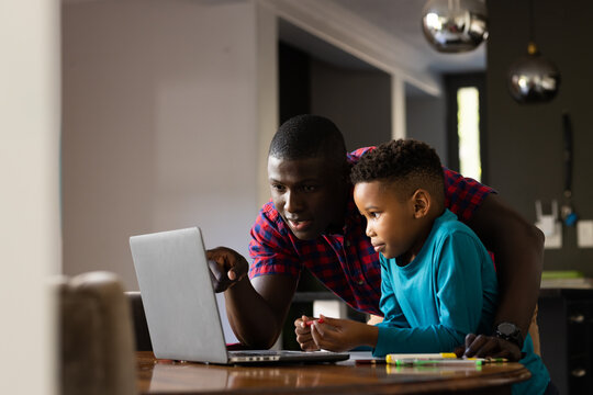 Image of smiling african american boy with father using laptop