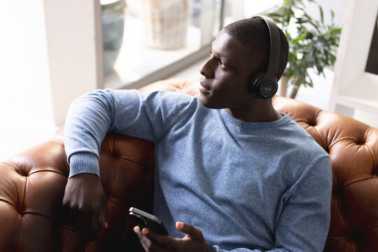 Image of relaxed african american in headphones sitting on sofa