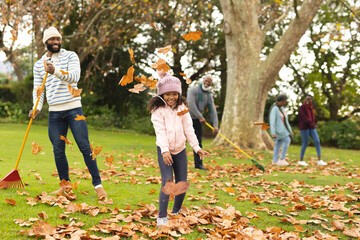 Fototapeta premium Image of happy african american multi generation family swiping leaves in autumn garden