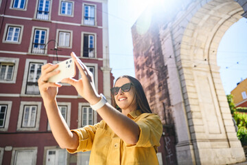 Overjoyed happy foreign woman tourist taking photo with trendy smartphone, walking in old town of...