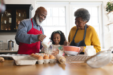 Image of happy african american grandparents and granddaughter baking in kitchen