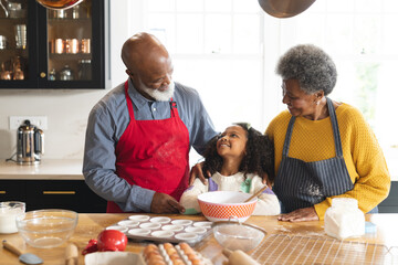 Image of happy african american grandparents and granddaughter baking in kitchen - Powered by Adobe