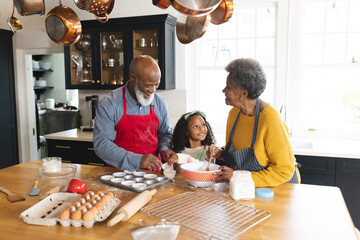 Image of happy african american grandparents and granddaughter baking in kitchen