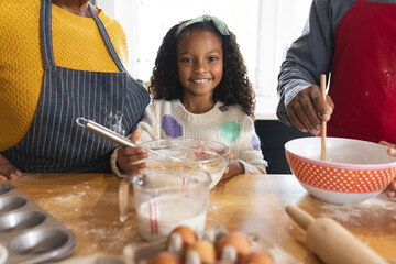 Image of happy african american grandparents and granddaughter baking in kitchen