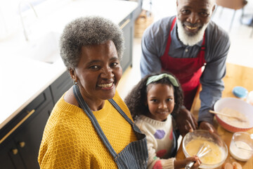 Image of happy african american grandparents and granddaughter baking in kitchen - obrazy, fototapety, plakaty