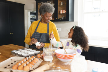 Image of happy african american grandmother and granddaughter baking in kitchen