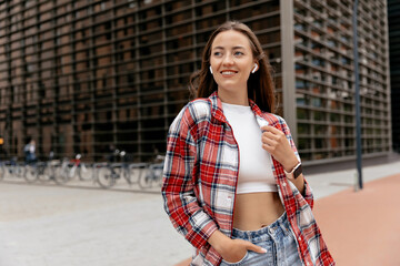 Happy adorable woman with wonderful smile wearing shirt, top and jeans walking on business district...