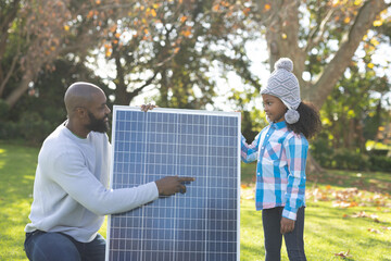 Image of happy african american father showing solar panels to daughter