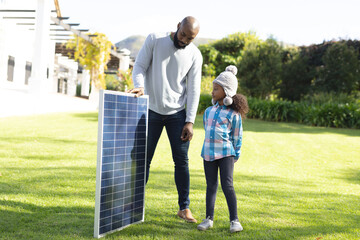 Image of happy african american father showing solar panels to daughter