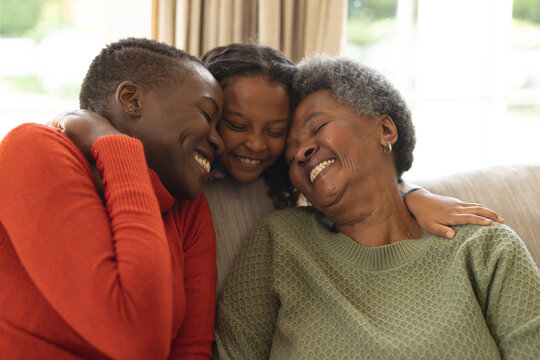 Image of happy african american three generation women sitting on sofa and embracing