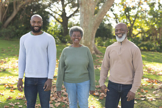 Image of happy african american parents and adult son posing in garden