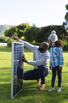 Vertical image of happy african american father showing solar panels to daughter