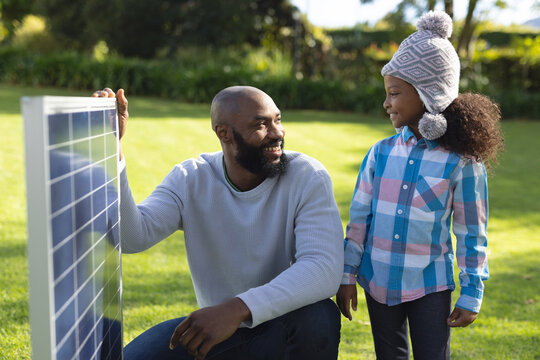 Image of happy african american father showing solar panels to daughter