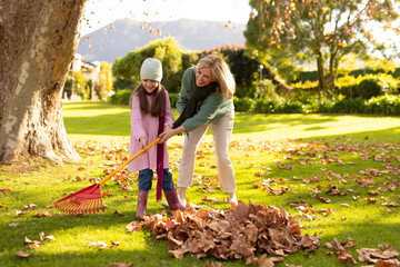 Image of happy caucasian grandmother and granddaughter swiping leaves in garden