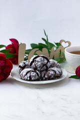Treats on a white table. Chocolate cracks cookies, a cup of tea and peonies