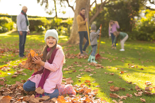 Image of happy caucasian girl playing with autumn leaves in garden