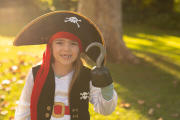 Image of happy caucasian boy in pirate costume in autumn garden