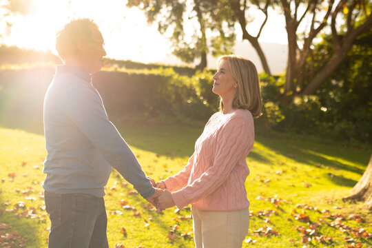 Image of happy senior caucasian couple holding hands in garden