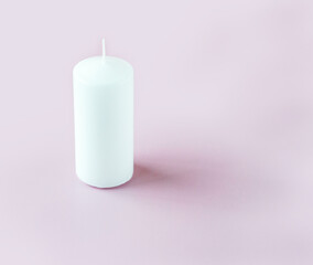 A white tall candle on the light pink background with copy space