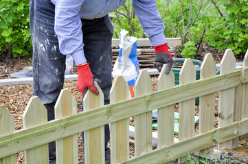Background of hands of man in red and black gloves installing  a wooden fence in the garden and...
