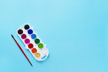 Watercolor paints with a brush on a blue background. Back to school concept. Horizontal orientation, top view, copy space.